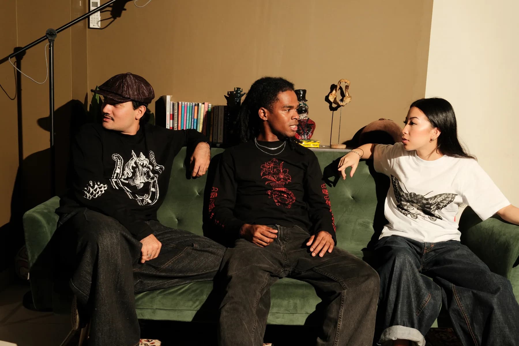 Three models share a relaxed moment on a green sofa.