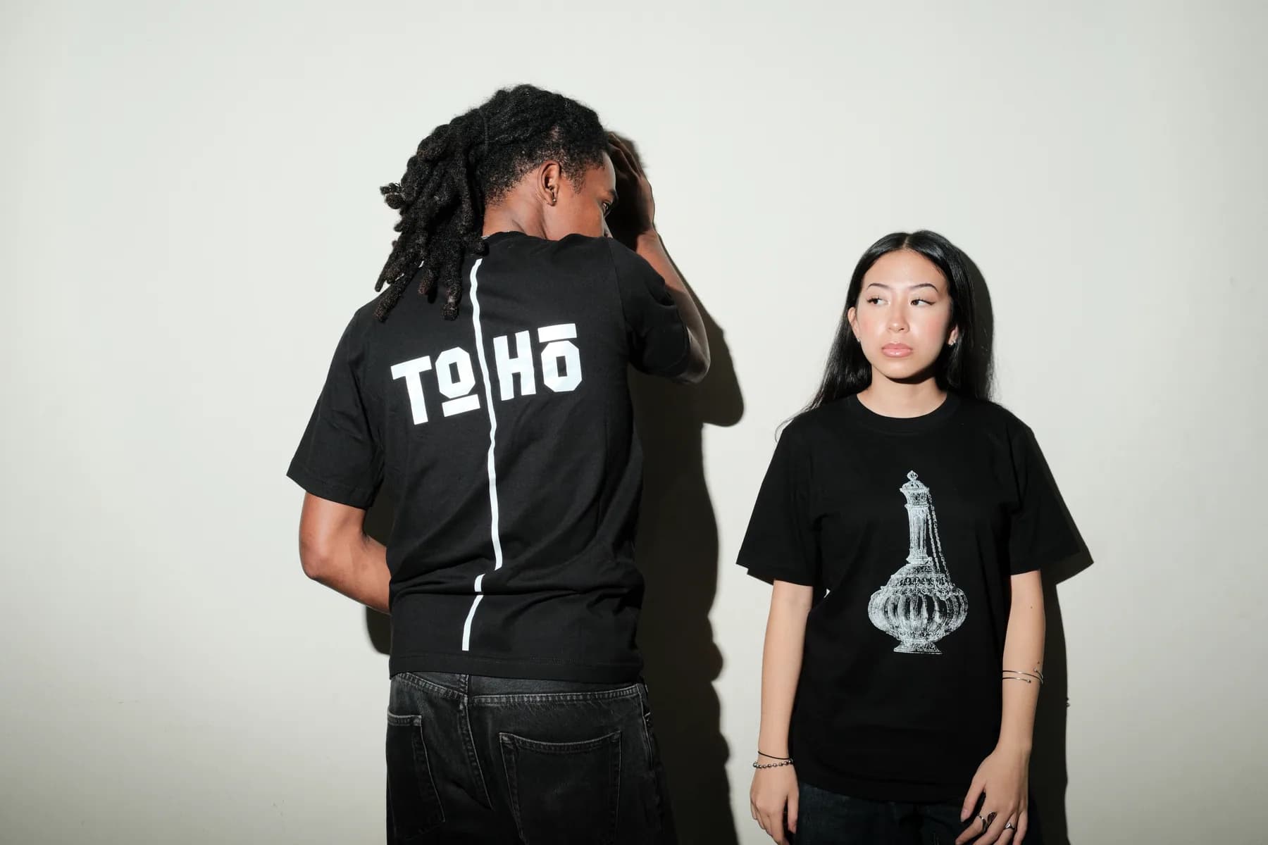Two models show the front and back of black TOHO graphic shirts in the studio.