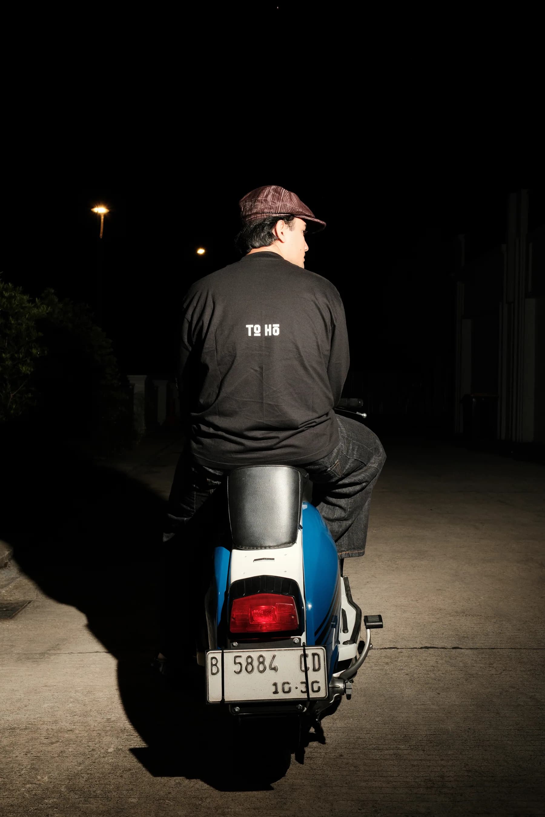 A model wearing a TOHO shirt at night on a scooter.